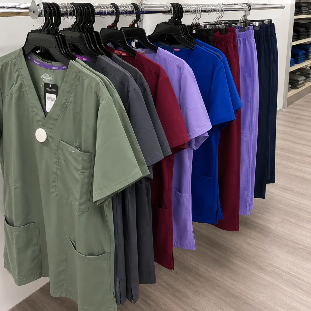 Wholesale medical scrub tops and pants in green, gray, burgundy, purple and blue displayed on a distributor clothing rack.